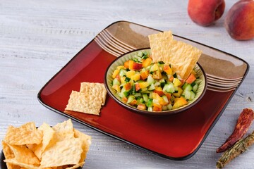 Salsa from fresh cucumber and ripe peach in a ceramic plate on a light wooden background. Served with wheat chips. Mexican cuisine.