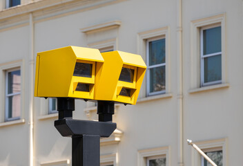 Low angle view of two bright yellow speed safety cameras against an urban background.