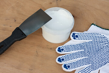 Builders kit, construction spatula, can of white putty, protective gloves, on plywood surface. Still life. Putty application kit.