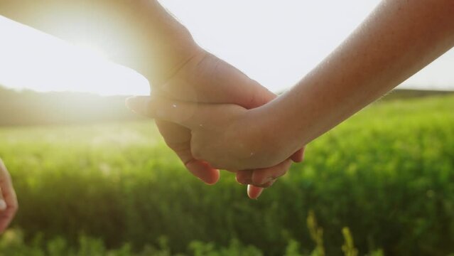 Hand of a man and woman holding on a blurred green field background against sunset. Couple goal.freedom