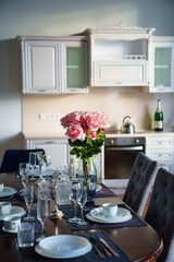 table with dishes and bouquet of roses in the bright kitchen of the living room 