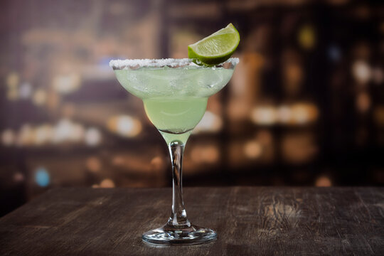 Margarita cocktail with sliced and whole limes on wooden bar table. Mexican party background