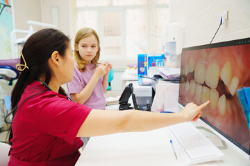 A pediatric dentist shows a small patient a photo of teeth on a computer screen.