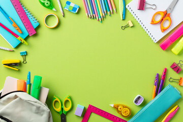 Back to school concept. Frame of colorful school stationery and backpack on green background.
