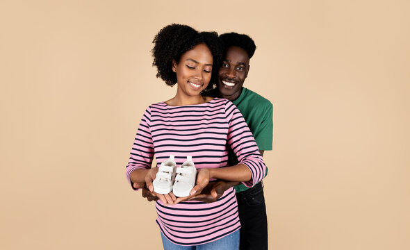 Smiling Young African American Man Hug Pregnant Woman With Big Belly, Mom Hold Small Shoes