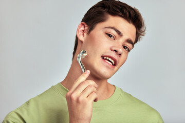 A young handsome guy with brown hair doing self-care routine using a face massage roller in a studio. Caucasian man caring for the skin to maintain his youthful and healthy appearance. Men's skincare.