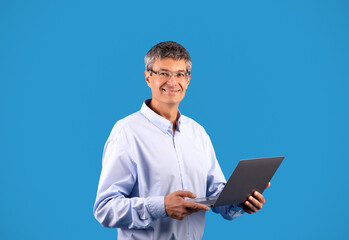 Obraz na płótnie Canvas Happy Mature Man Holding Laptop Computer Standing On Blue Background