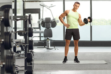 Fototapeta na wymiar Fit young man in sportswear exercising with a dumbbell at a gym