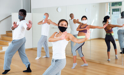 Multiethnic group of adult people wearing face masks for viral protection practicing active dancing in class