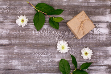 Composition with a gift wrapped in kraft paper, a green branch and white chrysanthemum flowers on a gray bleached wooden table. Copy space,flat lay