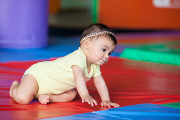 Beautiful ten months baby girl crawling on a colorful background. Early stimulation for toddlers concept.