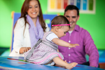 Beautiful ten months baby girl playing with her parents on background. Early stimulation for...