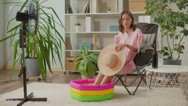 Sad Young Woman in a Beach Hat Resting at Home among Houseplants and Dreaming about Vacation, Woman Imagines she is Relaxing on the Sea, Woman Sitting on Armchair and her Legs is in Inflatable Bath