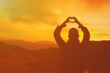 I love nature. Woman on a mountain looking out into the distance making heart symbol. 