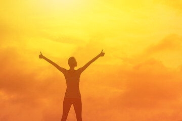Female stands, arms outstretched, silhouetted against vibrant sunset sky. Silhouetted Figure Embracing the Setting Sun in Success