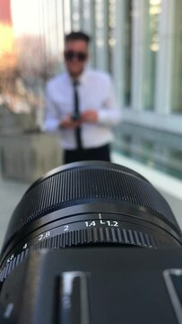 Detail of camera and objetive in a photoshoot with a professional, attractive and confident young businessman with phone, white shirt and black tie