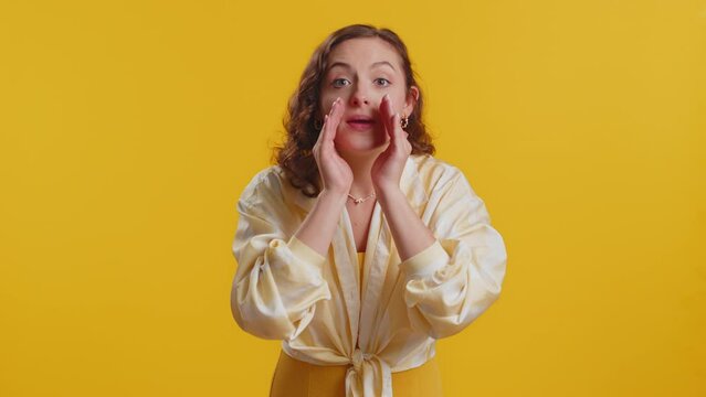 Keep my secrets, silence. Young woman whisper news rumors holding hands near mouth, share gossip, quiet. Girl telling interesting confidential story isolated on yellow studio background. Lifestyles