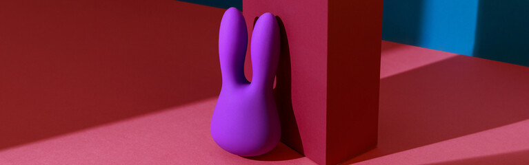 Violet dildo vibrator for clitoris with pink gift box on colored background. Sex toy for adult