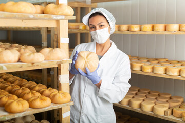 Focused Asian woman engaged in cheesemaking dressed in white uniform with cap, gloves and mask...