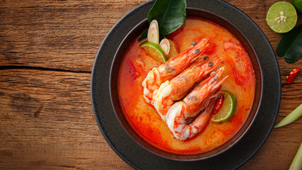 Taste of Thailand: Spicy and Sour Thai Tom Yum Goong Soup with Shrimp and Aromatic Ingredients on Black and Wooden Background