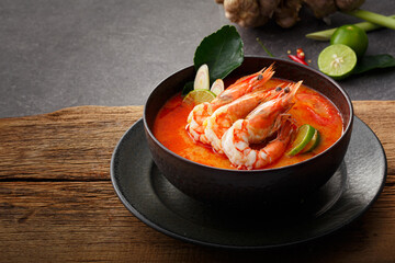 Taste of Thailand: Spicy and Sour Thai Tom Yum Goong Soup with Shrimp and Aromatic Ingredients on Black and Wooden Background