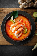 Taste of Thailand: Spicy and Sour Thai Tom Yum Goong Soup with Shrimp and Aromatic Ingredients on Black and Wooden Background
