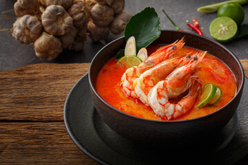 Taste of Thailand: Spicy and Sour Thai Tom Yum Goong Soup with Shrimp and Aromatic Ingredients on Black and Wooden Background