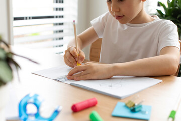 A cute boy makes a drawing with a ruler and pencil. Home lessons. Geometry and drawing.