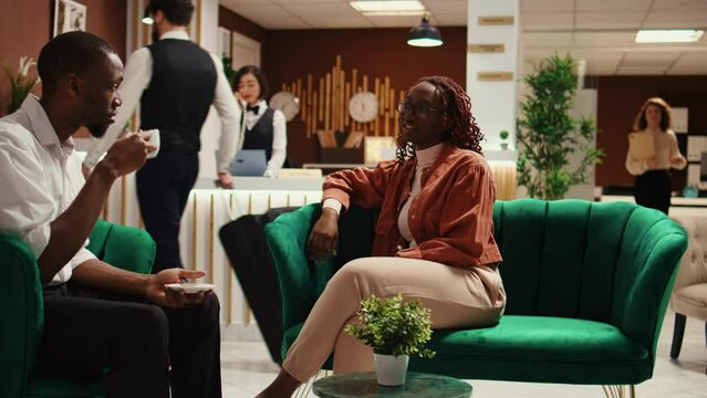 Collaborators in business trip sitting in stylish hotel foyer waiting to be checked in. Management executive partners enjoying cup of coffee in resort lobby while being booked in