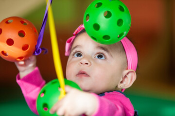 Beautiful ten months baby girl playing with colorful balls. Early stimulation for toddlers concept.