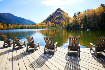 Beautiful autumn landscape. Wooden deck chairs on the lake shore. Outdoor recreation.
