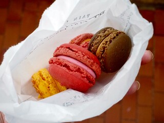 A white bag holding four colorful macarons from a boulangerie in Paris.