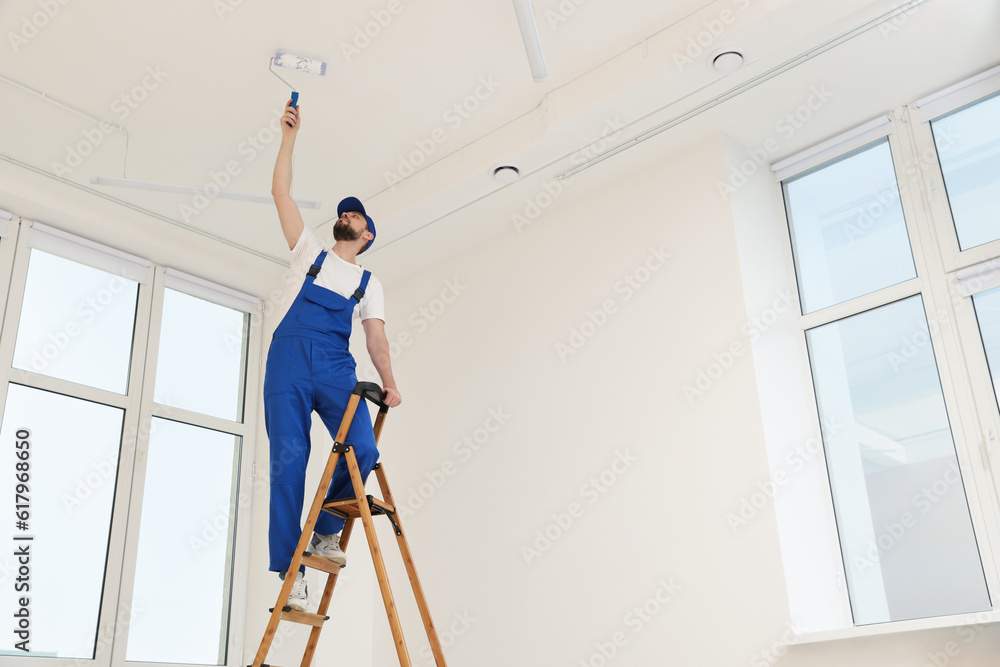 Canvas Prints Worker in uniform painting ceiling with roller on stepladder indoors, low angle view