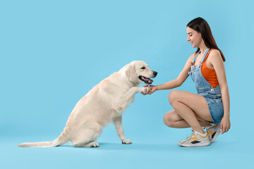 Cute Labrador Retriever dog giving paw to woman on light blue background. Adorable pet