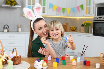 Mother and her son painting Easter eggs at table in kitchen