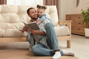 Little girl with her father reading book at home. International family