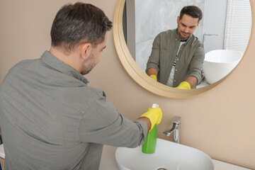 Man in rubber gloves with sprayer in bathroom