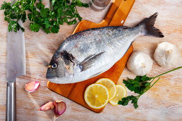 Fresh raw gilthead seabream with parsley, garlic, sliced lemon and spices on wooden kitchen table