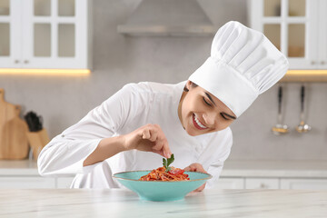 Professional chef decorating delicious spaghetti with parsley at marble table in kitchen