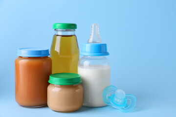 Healthy baby food, juice, milk and pacifier on light blue background