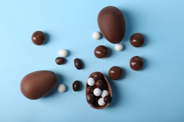 Tasty chocolate eggs and different sweets on light blue background, flat lay