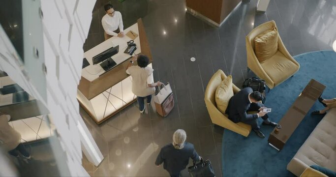 Top view of business people diverse group talking to hotel administrator indoors at reception desk. Travelling and accommodation concept.