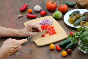 Woman cutting tomato for salsa sauce at wooden table, closeup