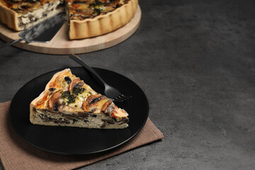 Piece of delicious quiche with mushrooms on dark grey table. Space for text