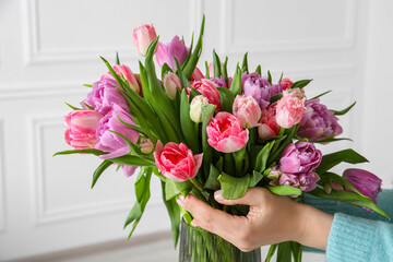 Woman putting bouquet of beautiful tulips in vase indoors, closeup