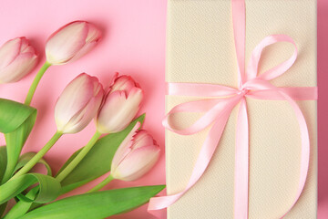 Beautiful gift box with bow and tulips on pink background, flat lay