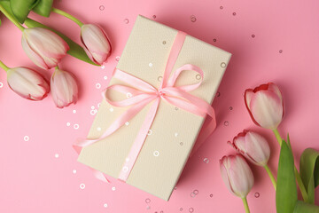 Beautiful gift box with bow, tulips and confetti on pink background, flat lay