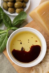 Bowl of organic balsamic vinegar with oil, basil, bread, cheese and olives on table, flat lay