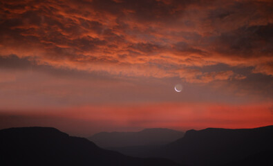 sunset sky with crescent moon over mountain silhouette