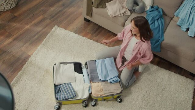 Top View of Young Woman Traveler Gathers Clothes for a Trip, Dancing, Packs Things into a Suitcase at Home.Road Trips. Remote Work and Travel.